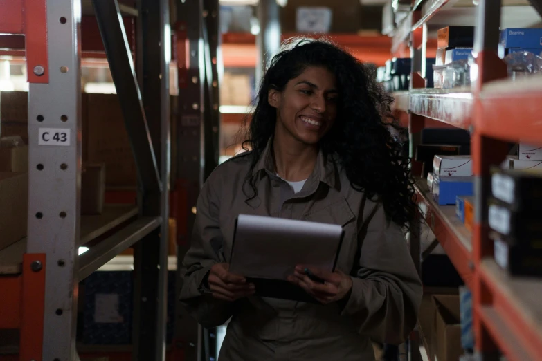 a woman is holding a laptop and standing in a warehouse