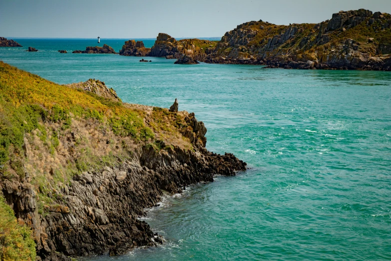 a body of water next to the shore with a green hillside in the background