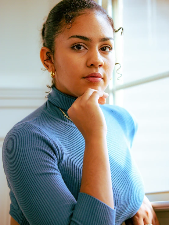 woman in blue sweater looking out window with hand on chin