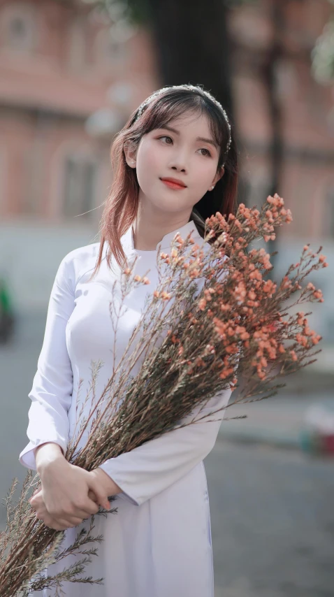 young asian woman holding dried flowers outside in white dress