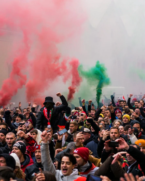 group of people waving and pointing at a red and green smoke bomb