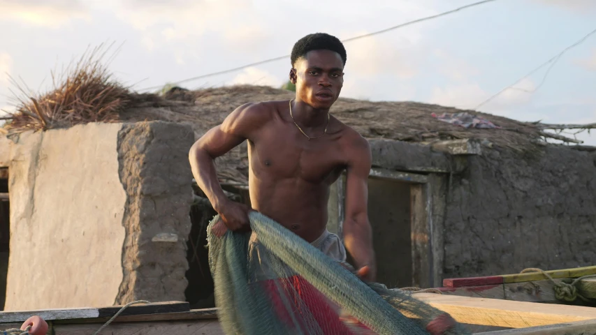 shirtless man holding onto a boat with two colors of fabric on it