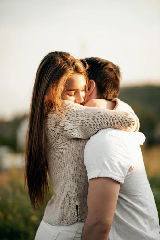 a young couple cuddling in an emce while standing in a field