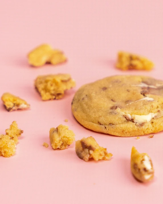 a chocolate chip cookie on pink surface with pieces missing