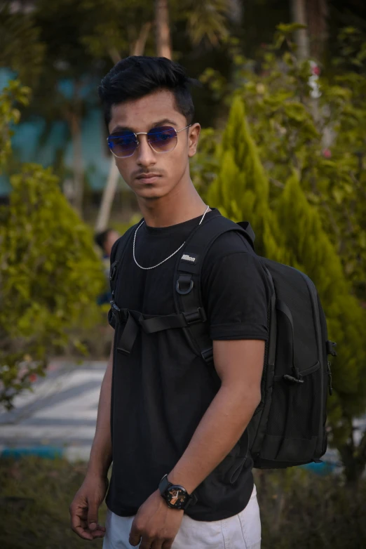 a man wearing sunglasses and a backpack standing in front of some trees