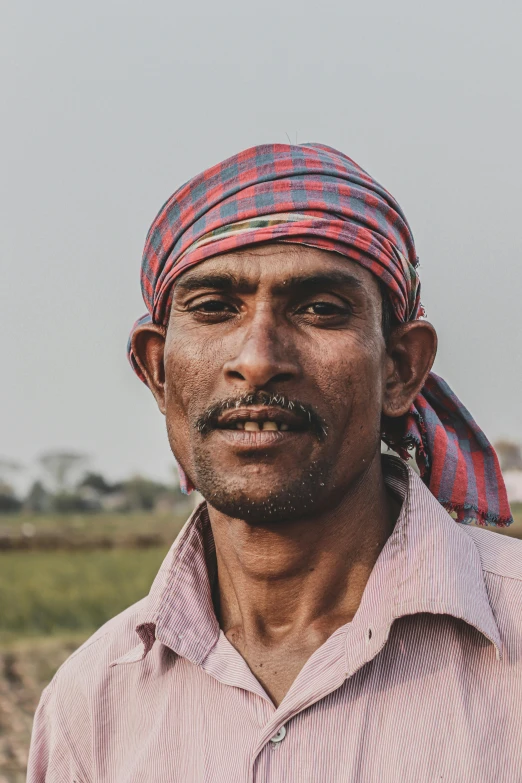 a man in red shirt and pink  bandana standing with his hat over his head