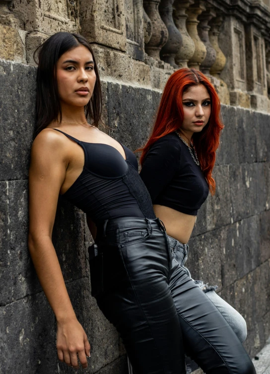 two pretty young ladies standing next to a stone wall
