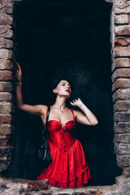 a woman in a red dress is leaning on an old brick wall