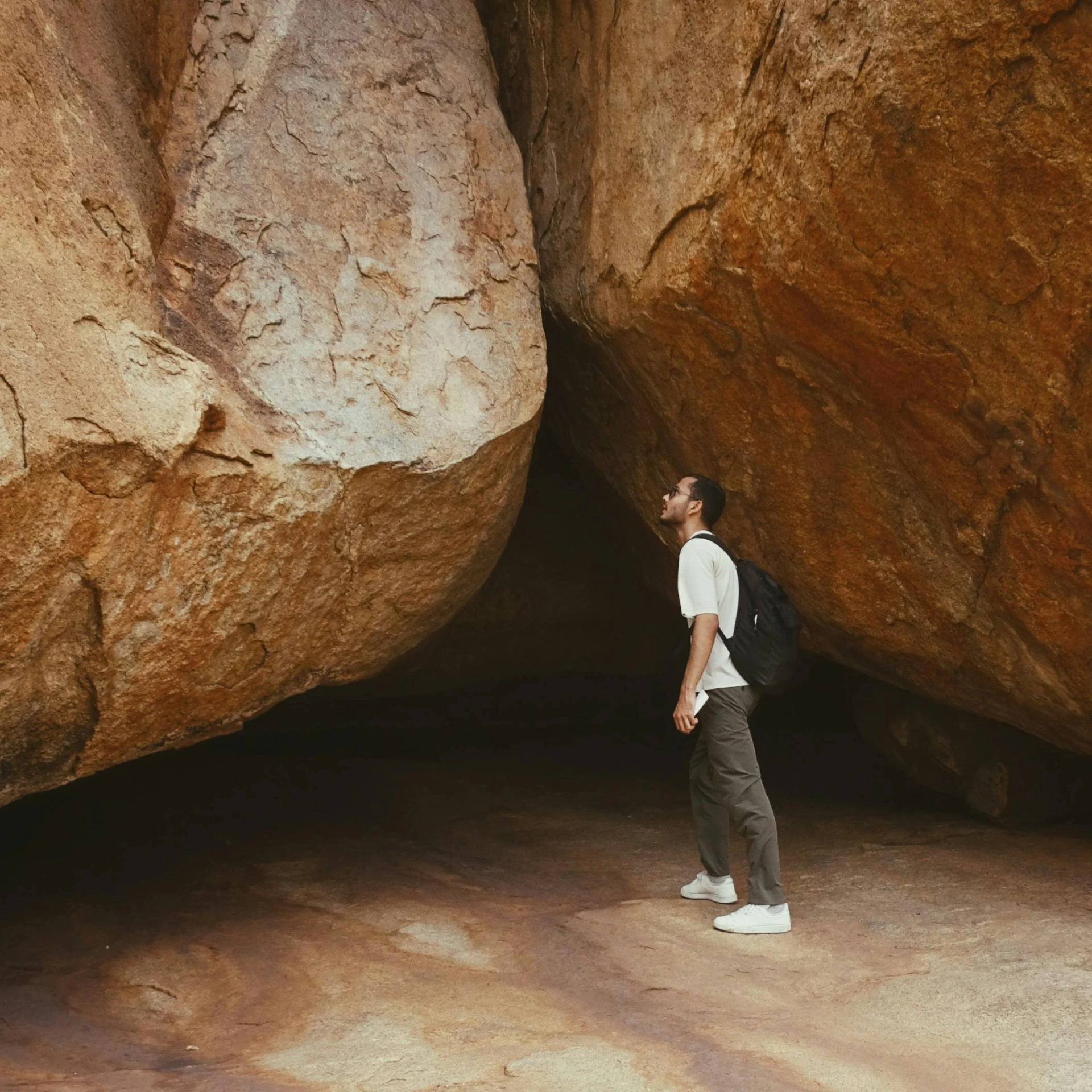 man in white shirt with backpack walking past large rocks