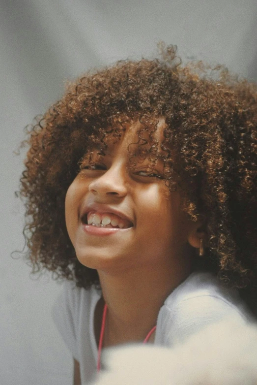 smiling female with large, curly afro hairs is wearing a gray sweatshirt