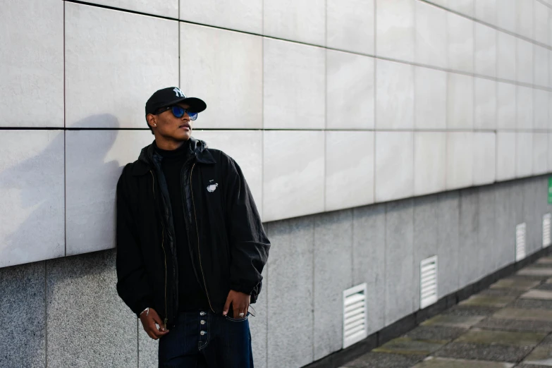 a man in black jacket standing against a wall