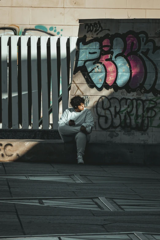 the man sits alone against graffiti covered wall