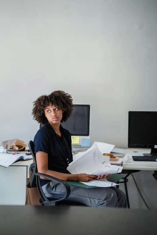 a woman sits at a desk with papers and a purse