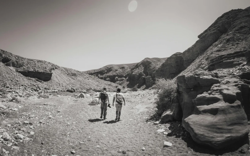 two men walk down a dirt path between rock formations