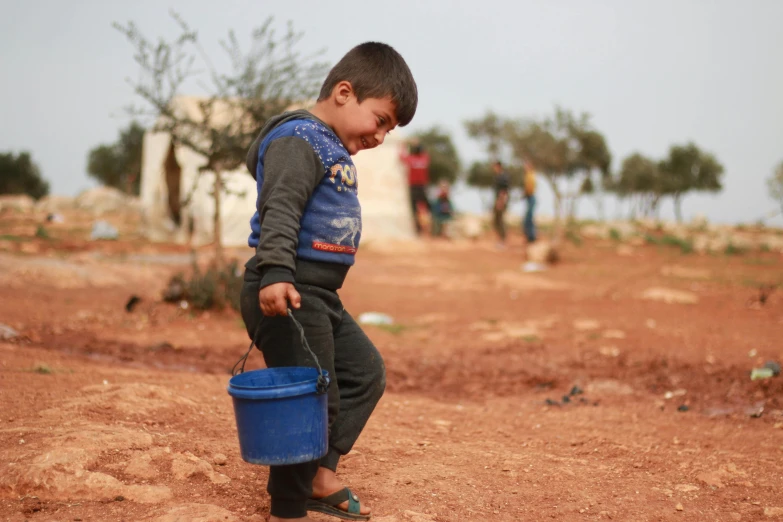 a boy is holding a blue bucket in the dirt