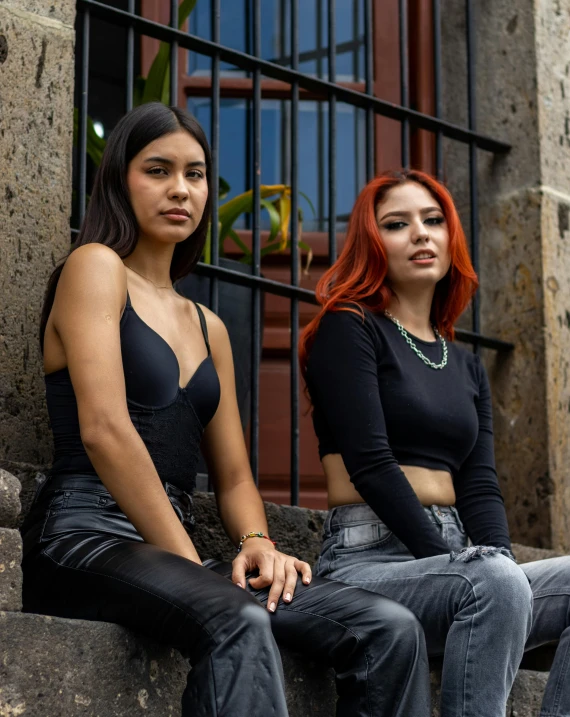 two girls sit on the concrete outside of a building