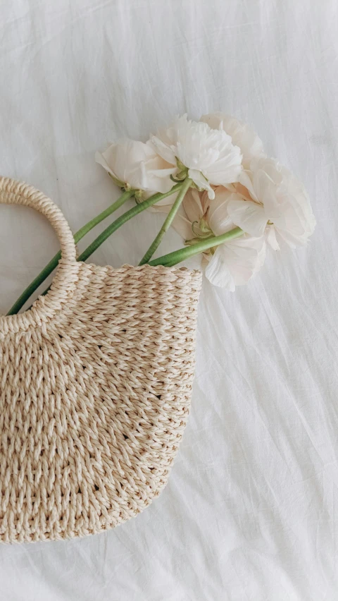 the handle of a woven straw purse sits next to a flower