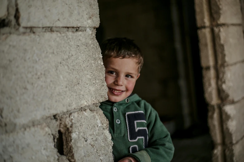 a boy in green shirt leans on wall with brick