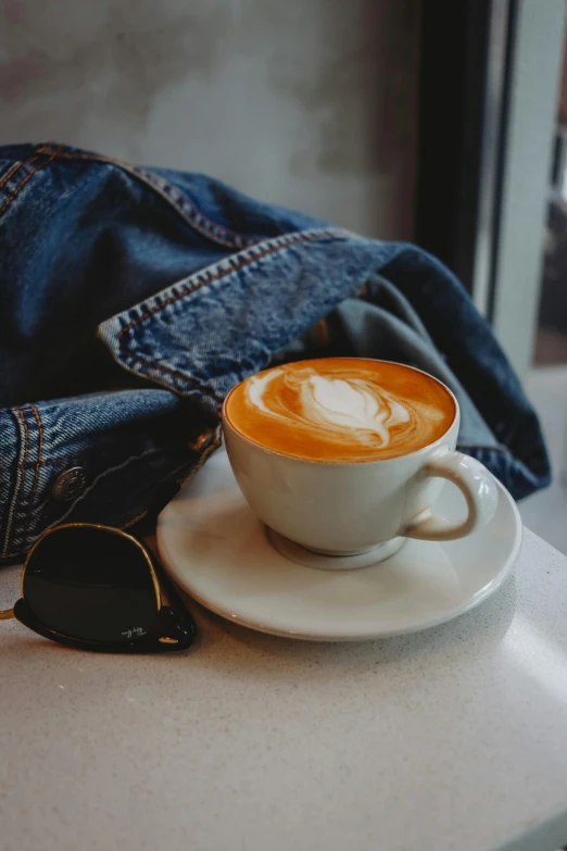 a cappuccino sits on a saucer near a jacket