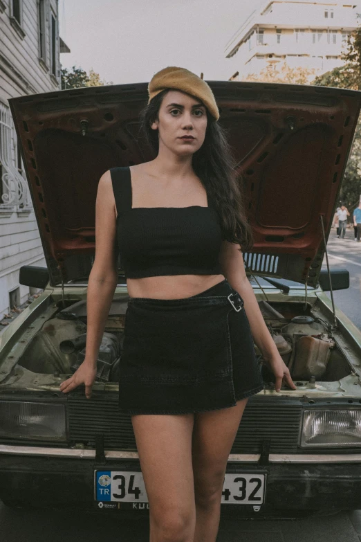 a woman posing next to a car with its hood open