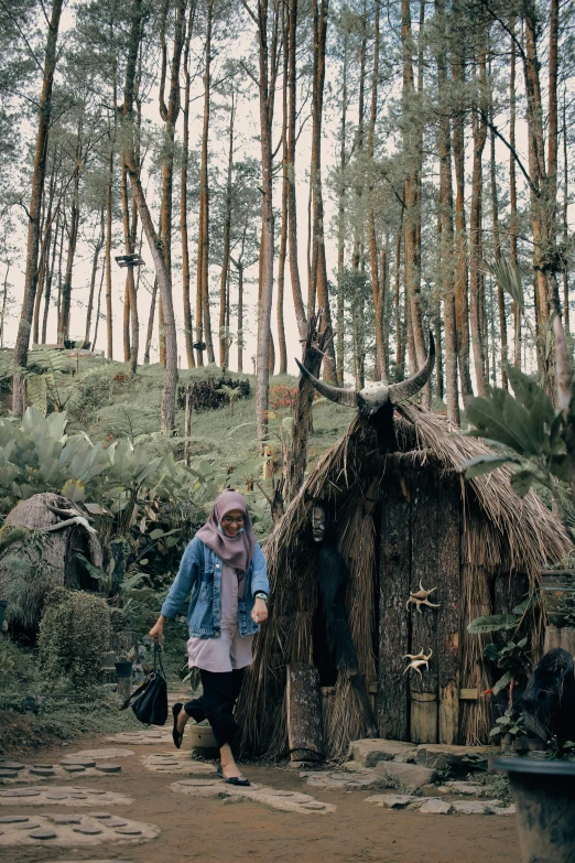 woman in pink outfit and blue jacket walking past a hut