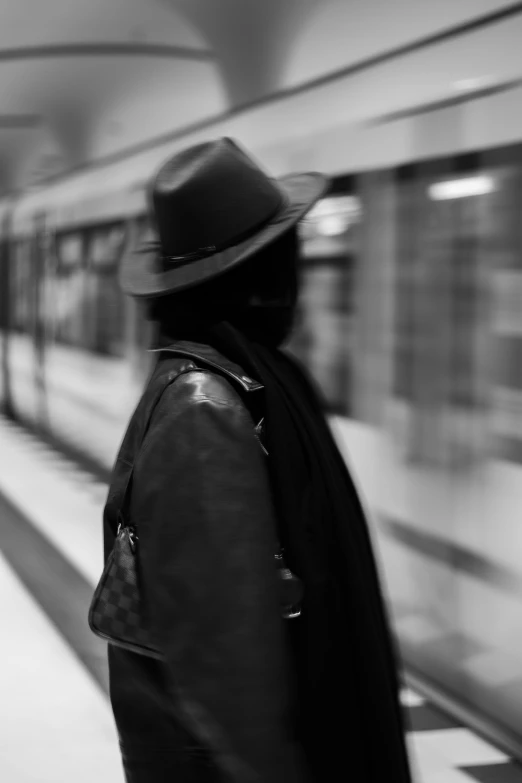 a person with a back pack and hat waiting on a train
