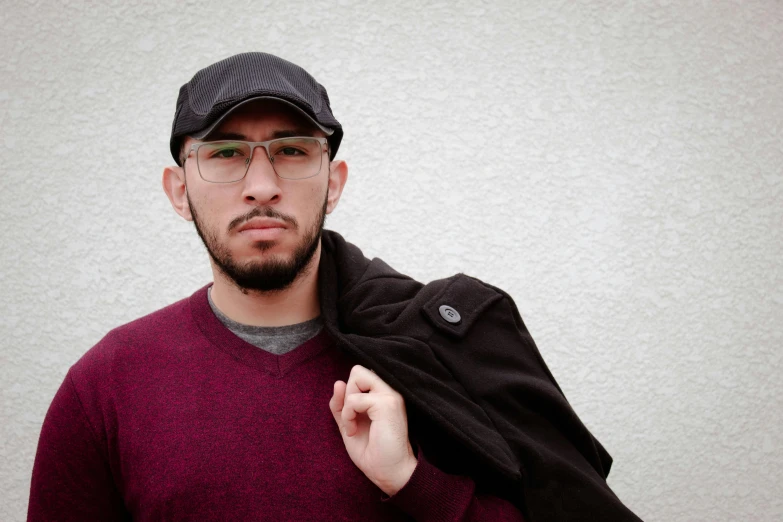 a man wearing glasses and a maroon sweater standing next to a white wall