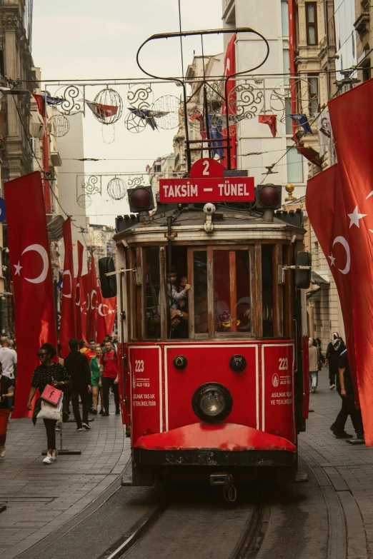 a red trolly bus traveling through the street filled with people