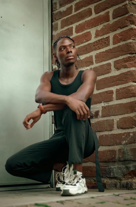 a black man is sitting on the ground in front of a brick wall