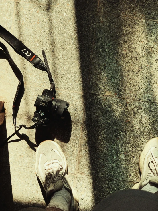 two persons standing on sidewalk with their feet propped up next to a camera