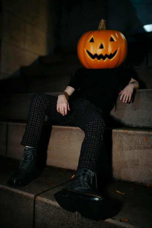 a man wearing a pumpkin mask sits on steps