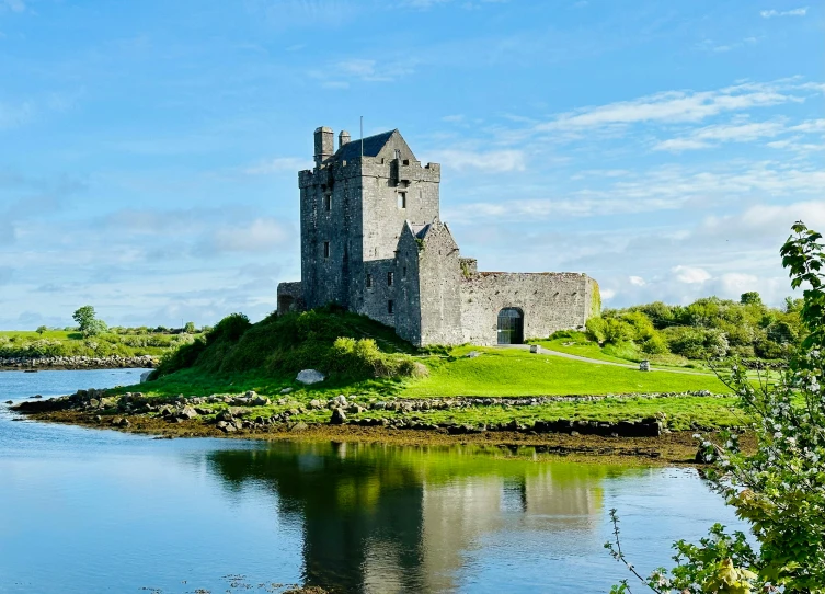 a castle sitting on top of a lush green hill next to water