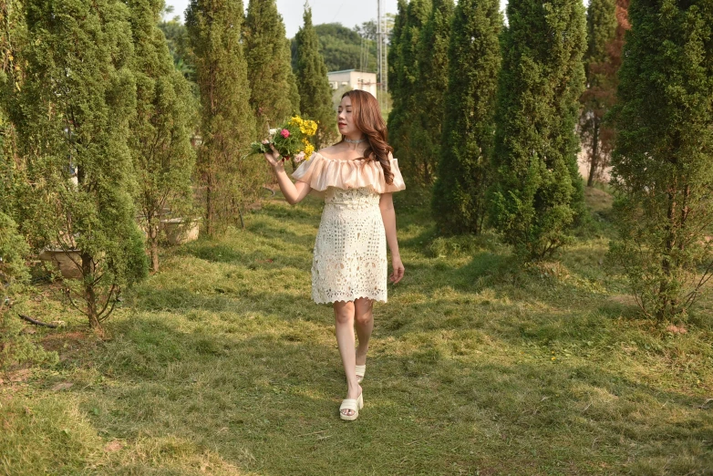 a woman walking down a grass covered field next to tall trees