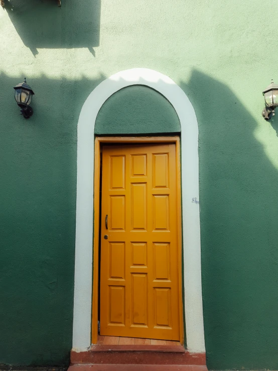 yellow door on green stucco wall with two light fixtures