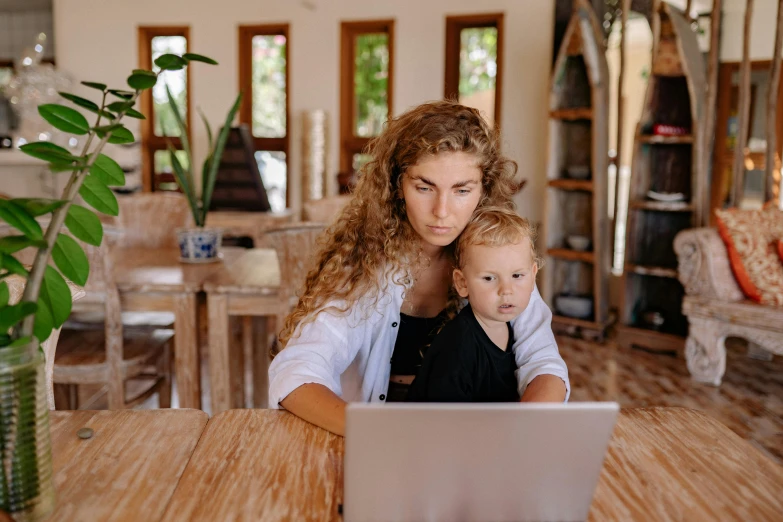 a woman and her child sit at a table in front of a laptop computer