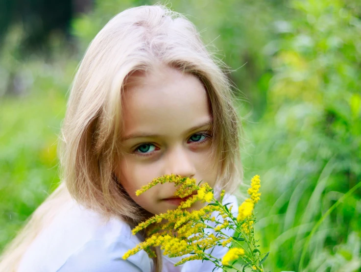 a little girl that is sitting in the grass with a flower