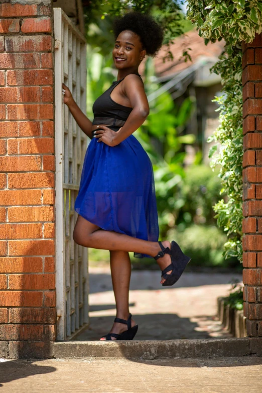 a woman in a blue dress stands near a gate