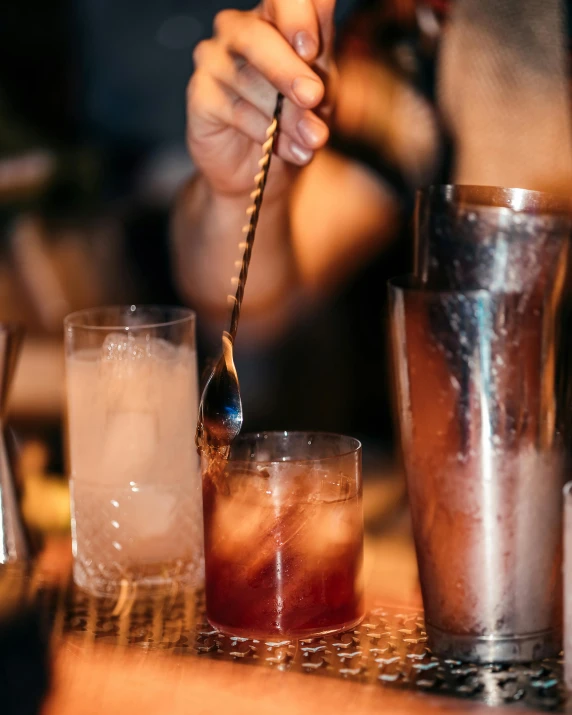 two drinks are on a bar with one being poured from a spoon