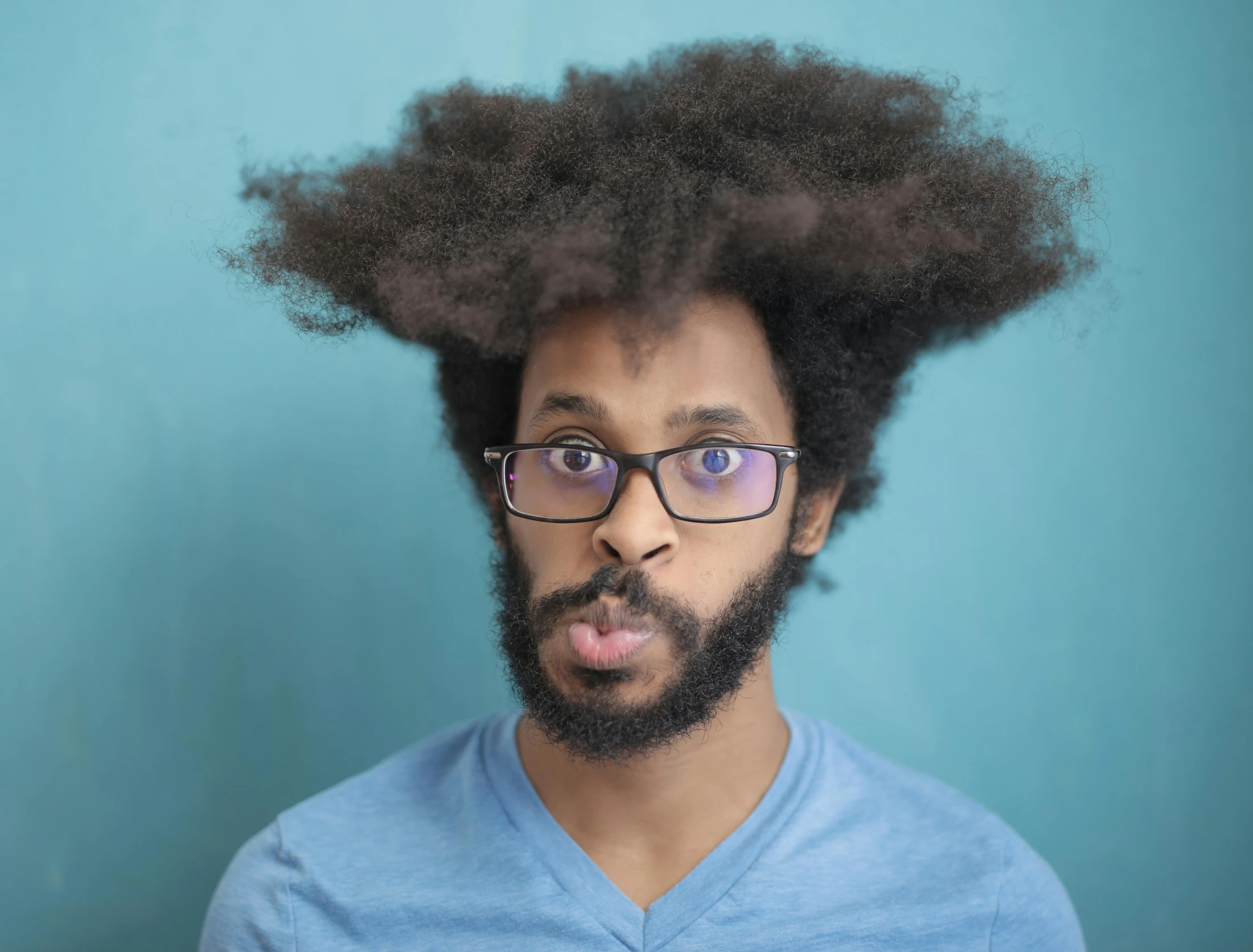 a man with glasses and beard with afro sticking out tongue