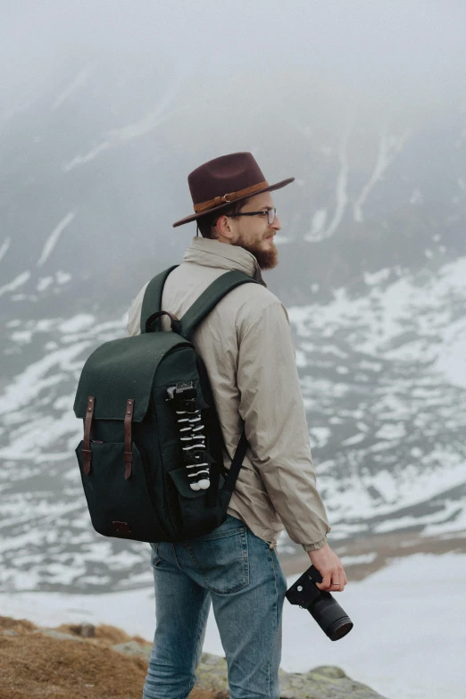 man with beard in hat and backpack standing on top of a mountain