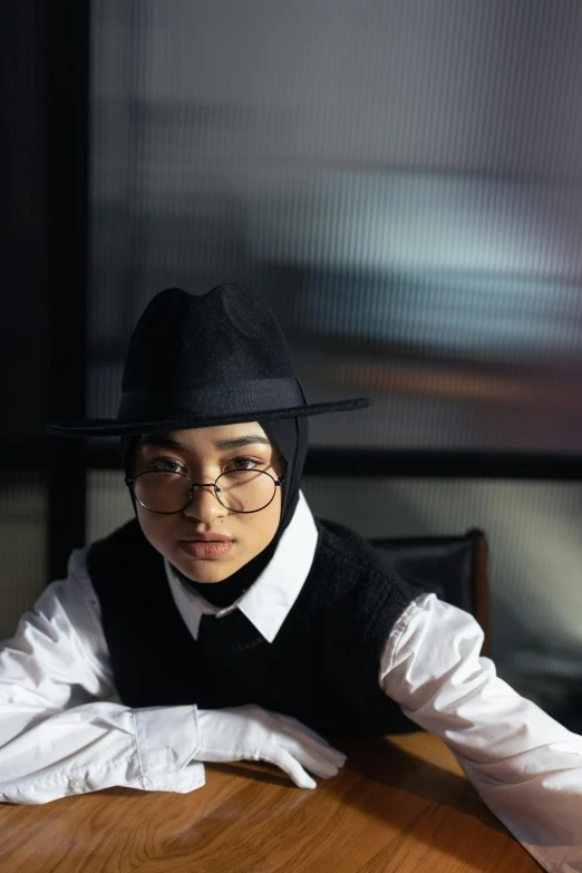 a person sitting at a table with a hat and eye glasses on