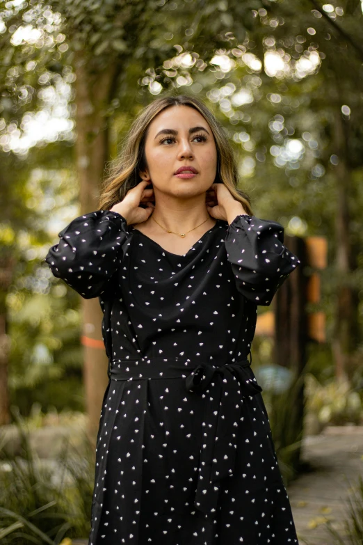 a woman in a dress standing outside wearing her hands behind her head