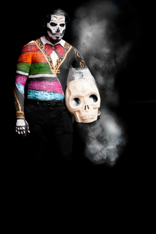 a man is holding a skeleton mask while wearing a rainbow colored sweater