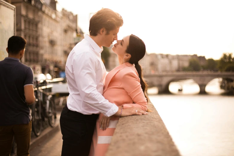 an asian couple kiss as they stand on a railing near water