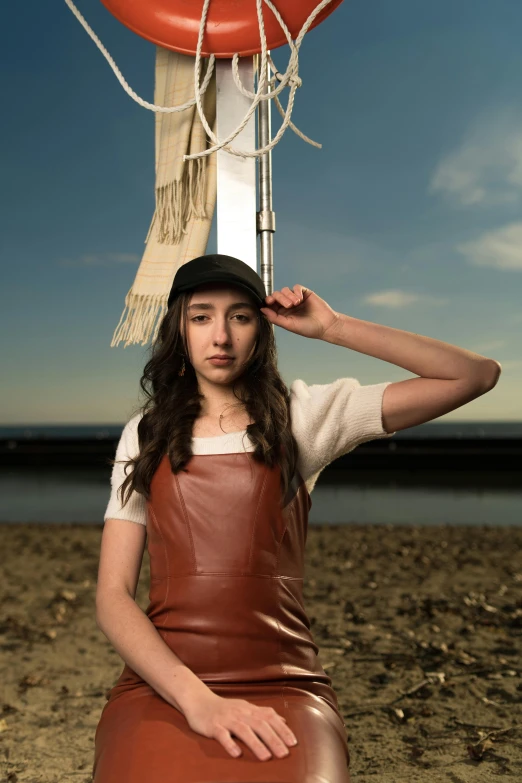 a woman is wearing a brown leather outfit while posing in front of a red ball and a white and gray flag on the beach