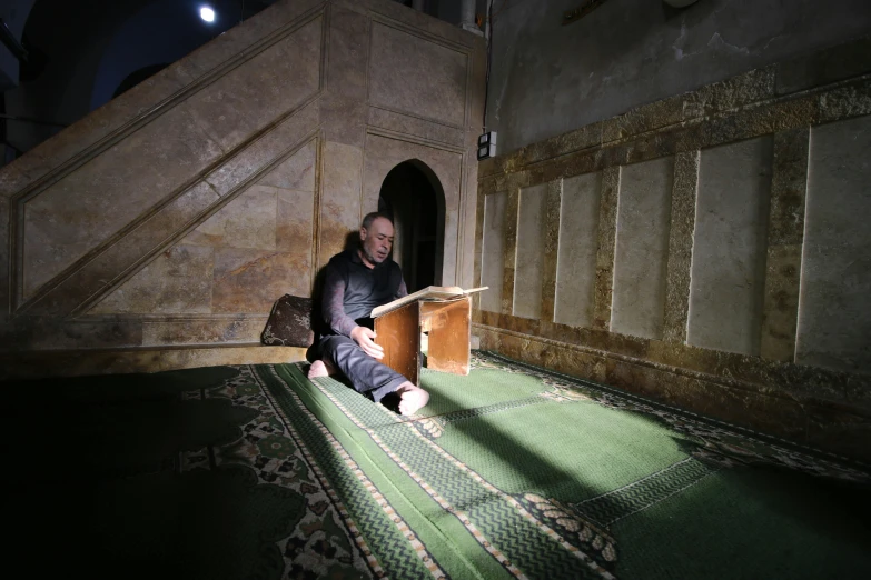 a man sits in a corner under a stair case