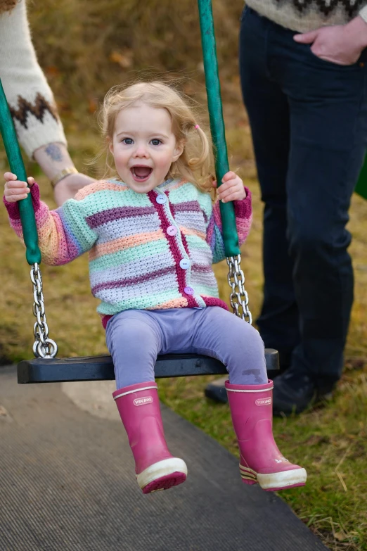 a child in pink boots sitting on a swing