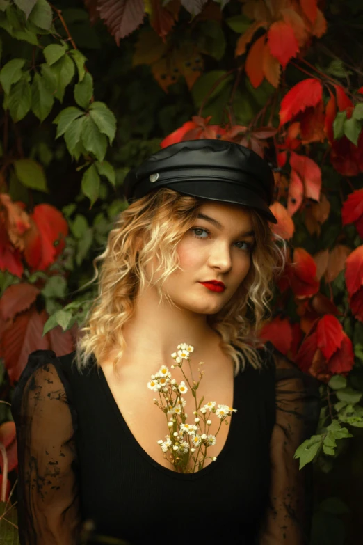 a woman is wearing a hat and holding flowers