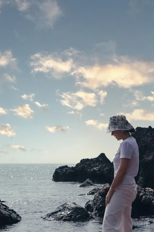 woman wearing a hat standing by rocks near the ocean