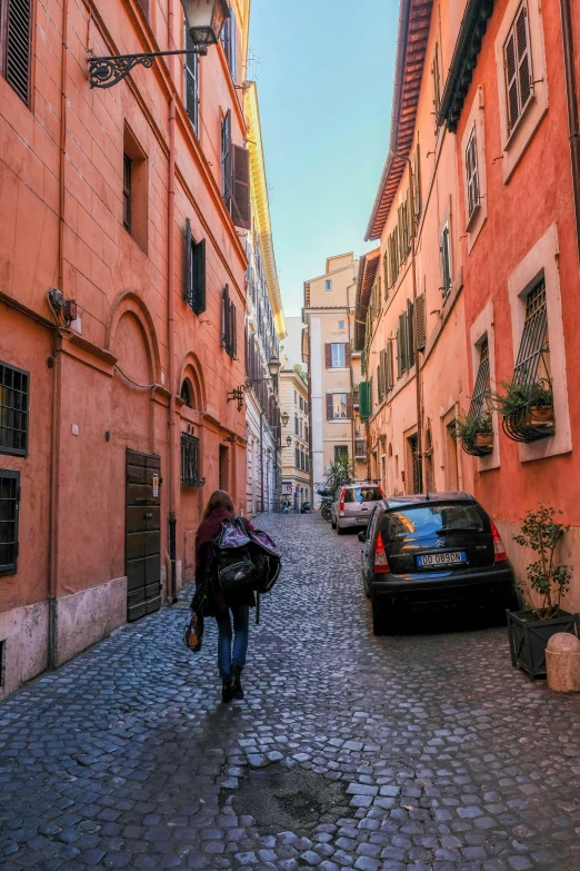 a cobblestone road is shown with pink buildings on both sides and cars parked on the side of the road